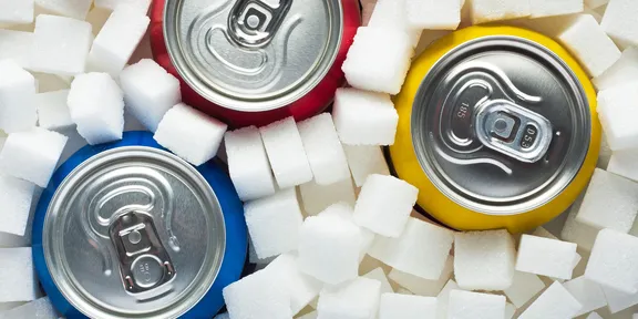 Three soft drink cans surrounded by sugar cubes
